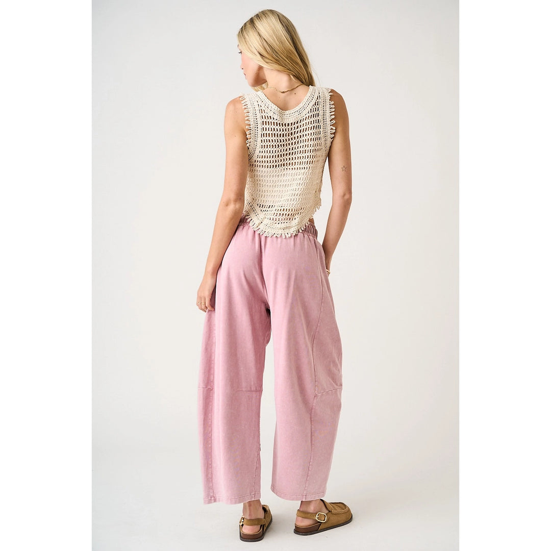 Woman wearing a sleeveless crochet top and pink pants on a white background
