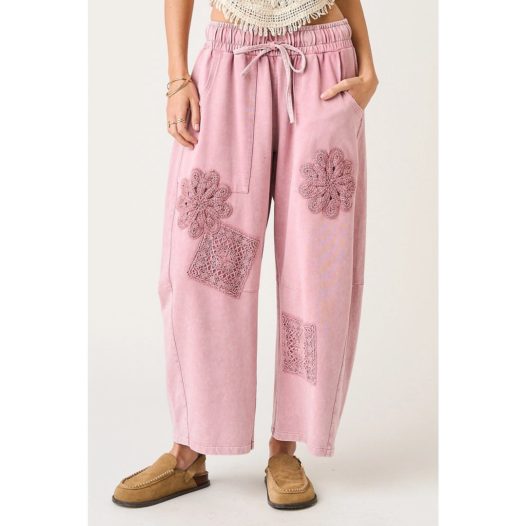 Pink pants with floral lace patches worn by a person on a white background