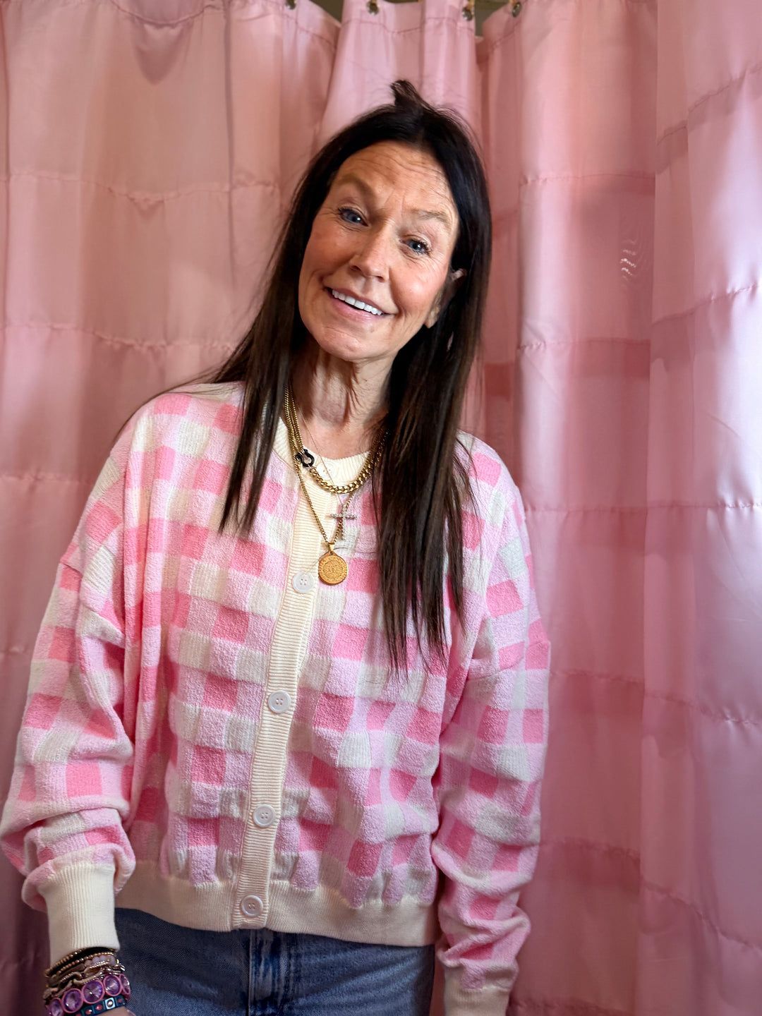 Woman wearing a pink checkered cardigan in front of pink curtains