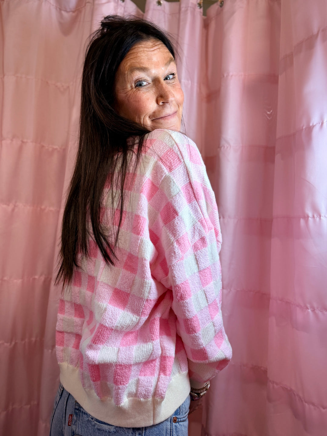 Person wearing a pink and white checkered shirt in front of a pink curtain