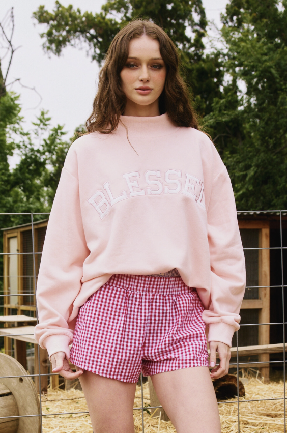 Woman wearing a pink sweatshirt and checkered shorts outdoors