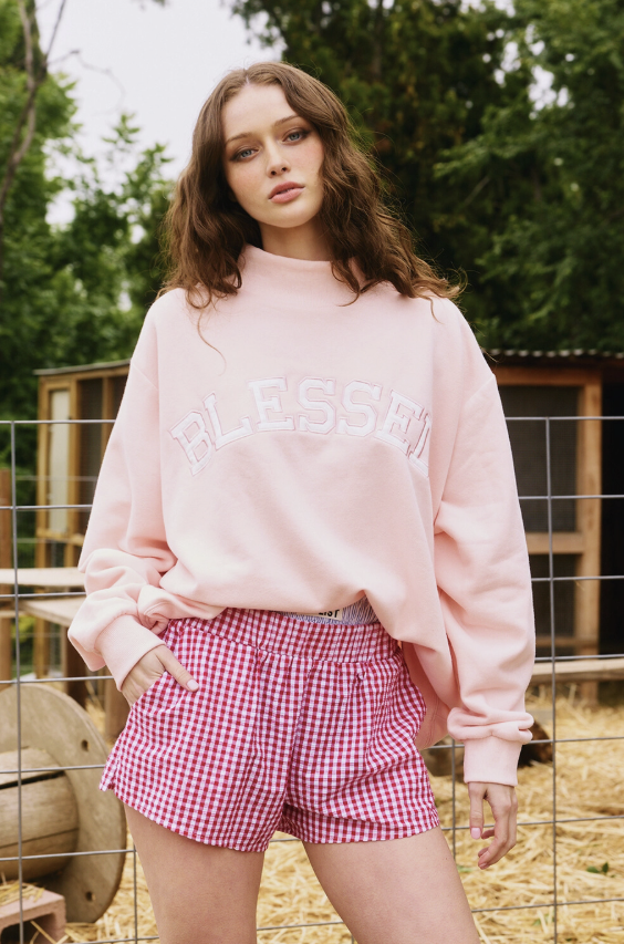 Woman wearing pink sweatshirt and checkered shorts outdoors