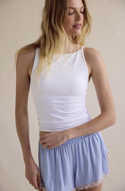 Woman wearing a white tank top and light blue skirt against a beige background