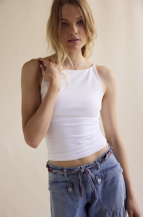 Woman wearing a white tank top and blue jeans against a beige background