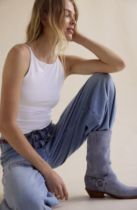 Woman wearing a white tank top and blue jeans with purple boots sitting on the floor.