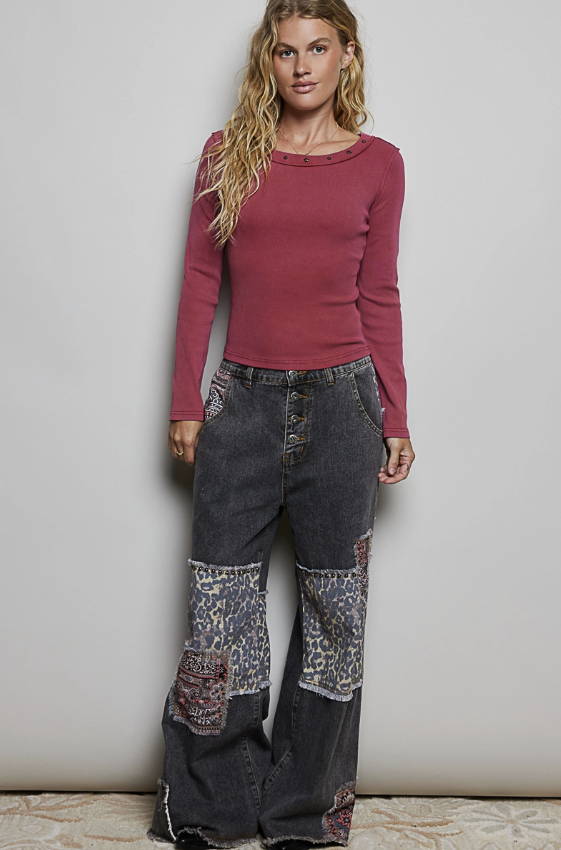 A woman modeling a long-sleeve crewneck top in dusty rose and wide-leg patchwork jeans with leopard-print and floral fabric panels, standing against a plain light gray wall.