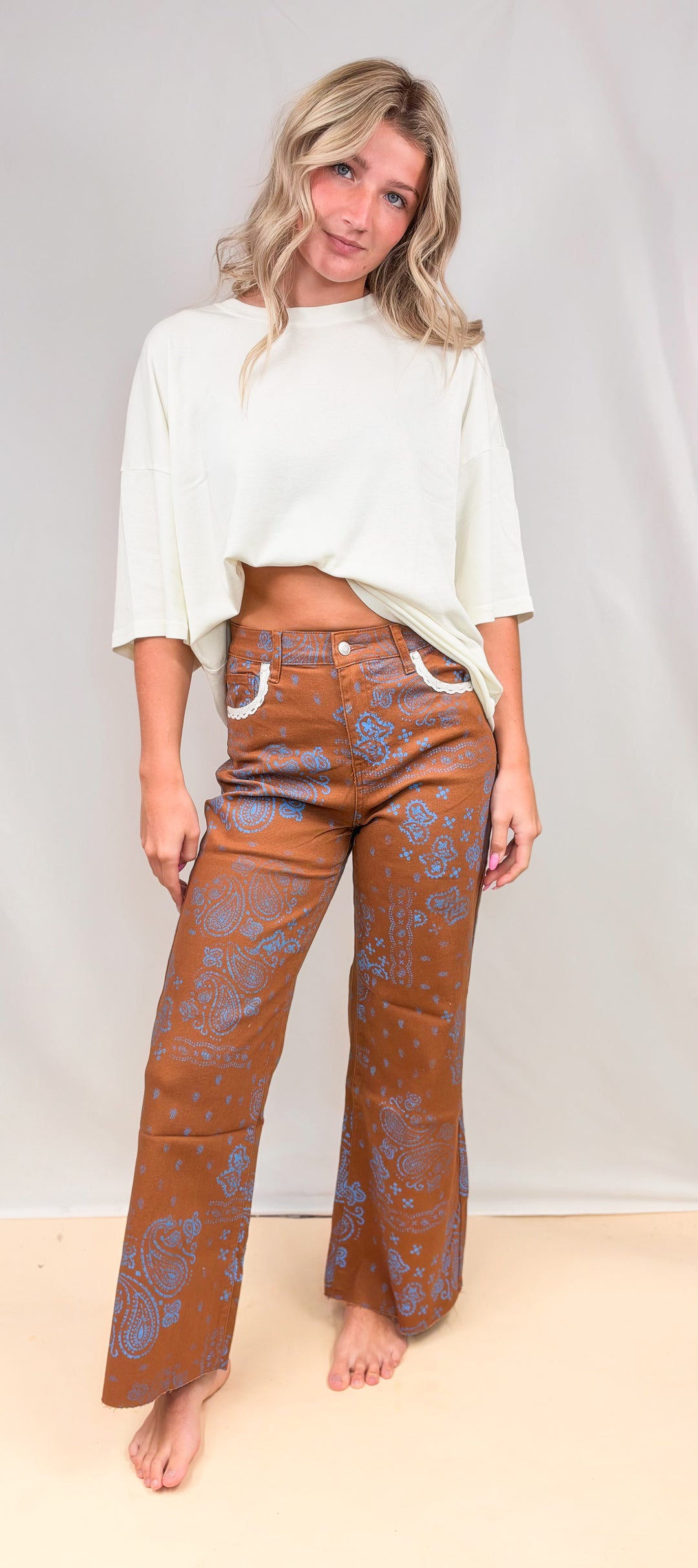 Woman wearing rust colored pants with blue paisley design and cream shirt on plain background