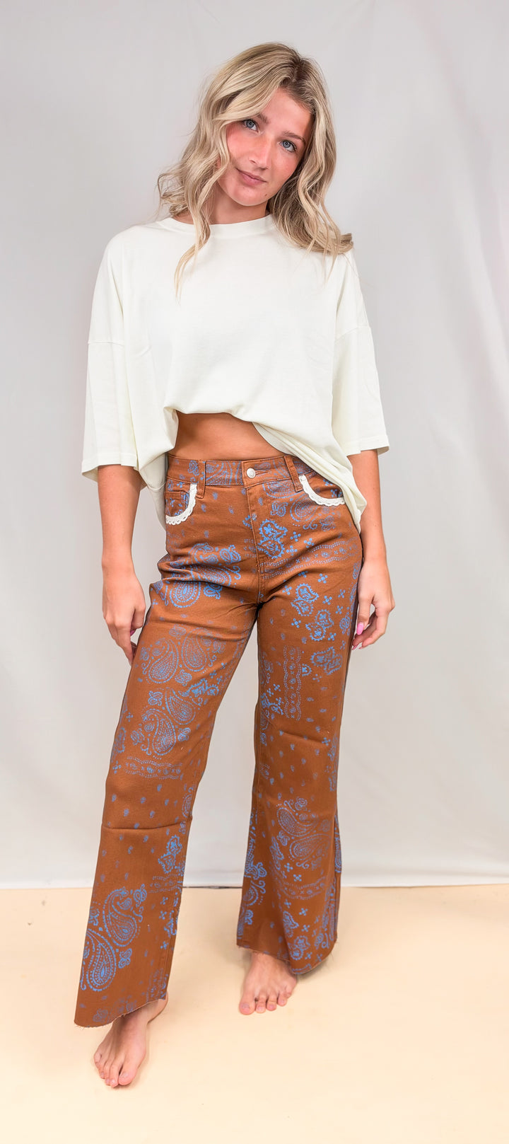 Woman wearing rust colored pants with blue paisley design and cream shirt on plain background