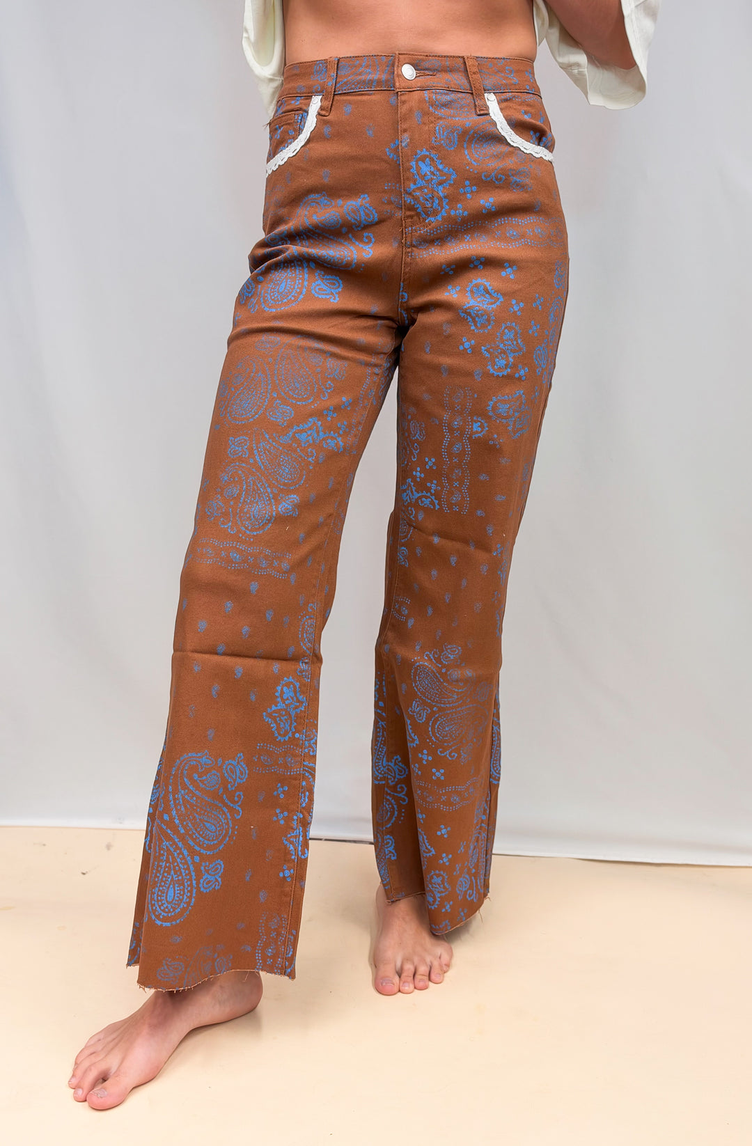 Woman wearing rust colored pants with blue paisley design and lace detail on plain background