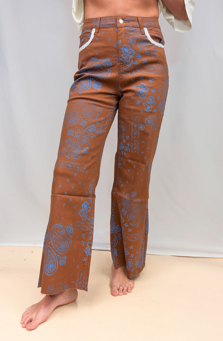Woman wearing rust colored pants with blue paisley design and lace detail on plain background