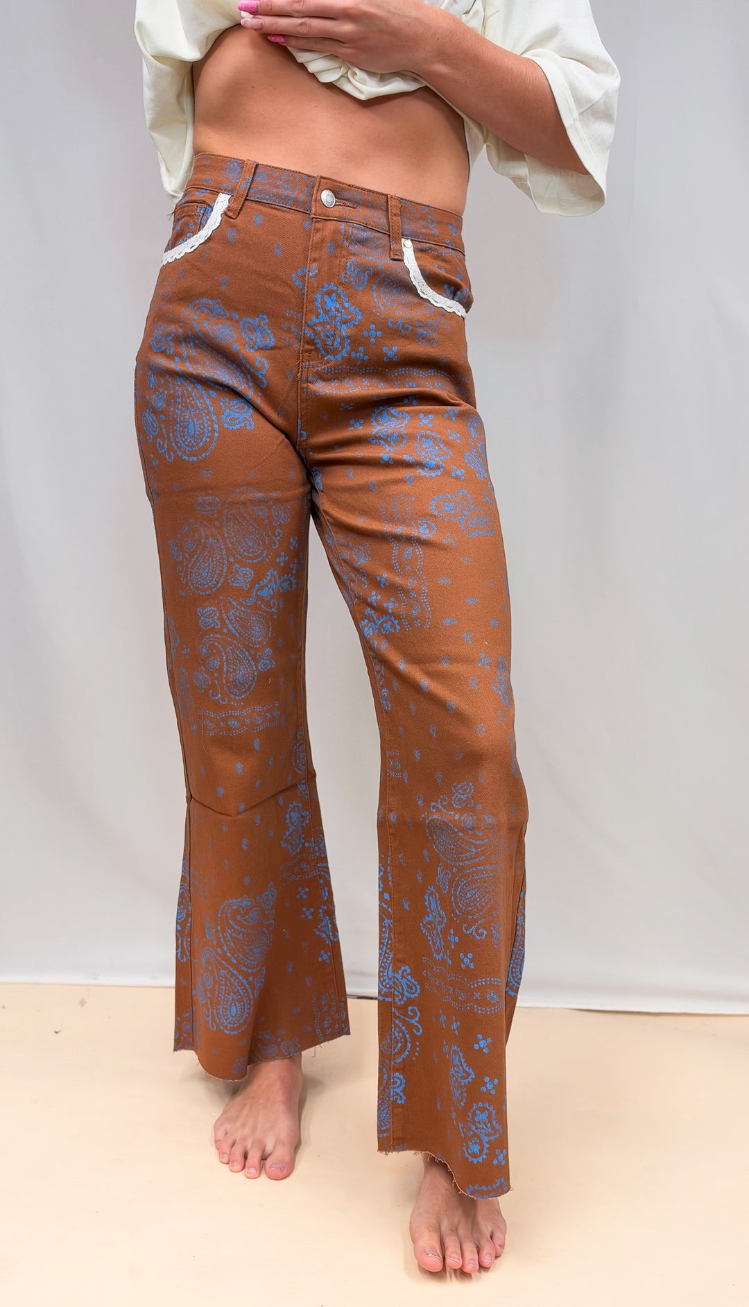 Woman wearing rust colored pants with blue paisley design and lace detail on plain background
