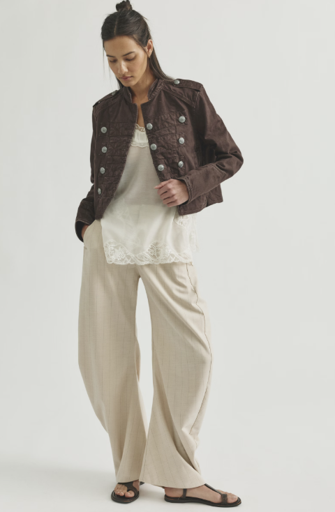 Woman wearing chocolate brown band jacket with beige tank and beige pants on white background