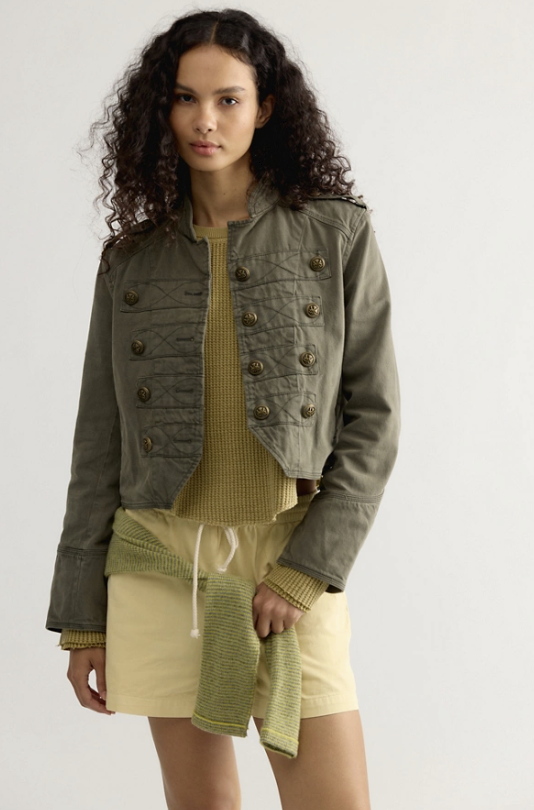 Woman wearing olive green band jacket with yellow top and skirt on white background