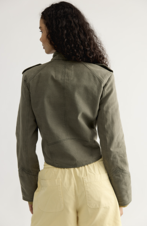 Woman shown from back wearing olive green band jacket and yellow shorts on white background