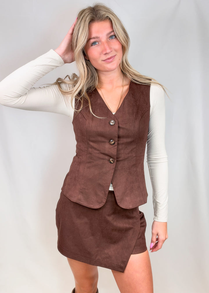 Woman wearing matching dark brown vest and skort set on plain background