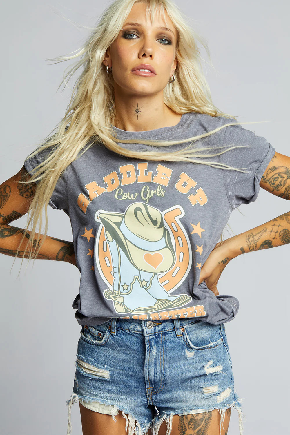 Woman wearing a graphic t-shirt with a cowboy hat design and text, standing against a plain background.
