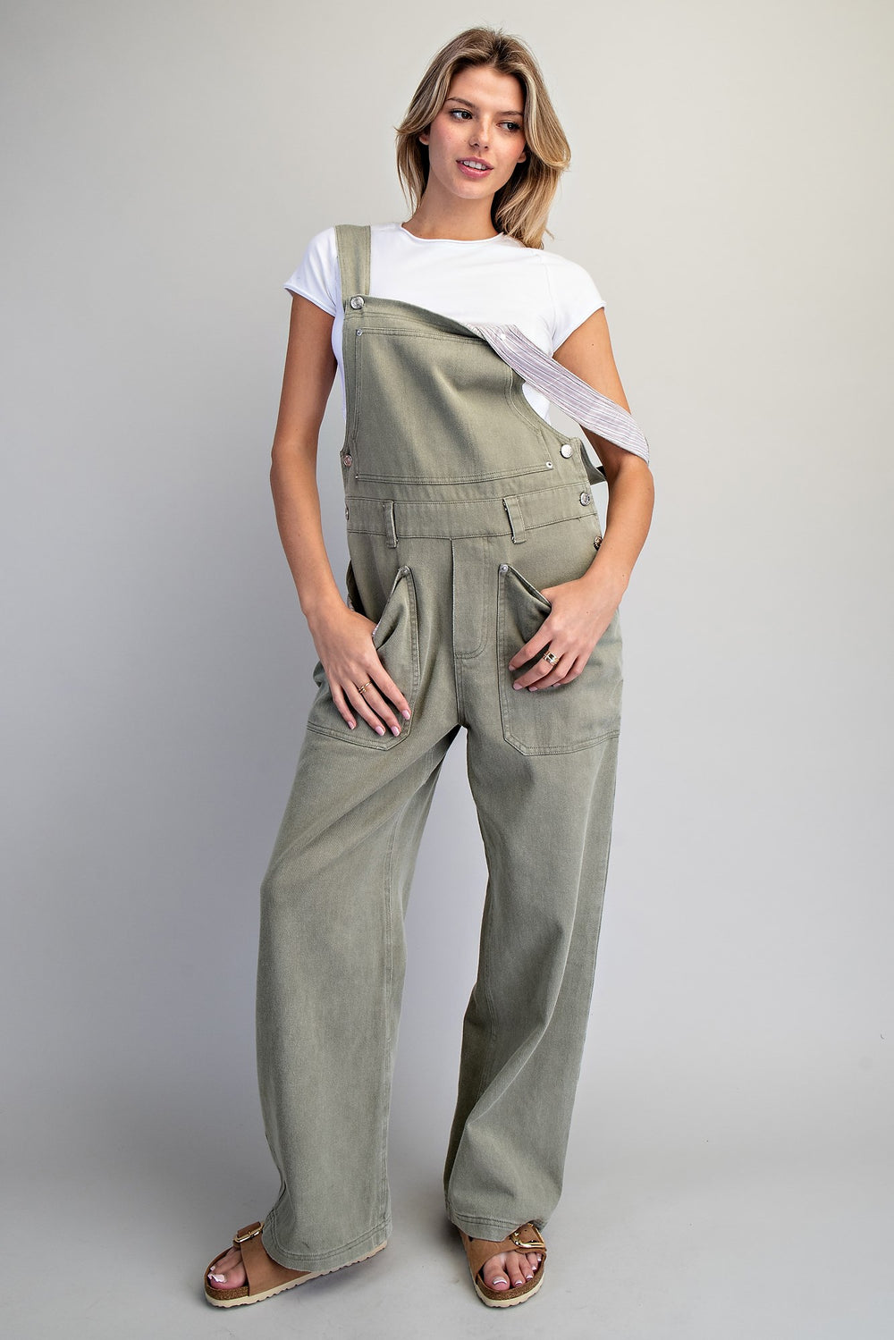 Woman wearing green overalls and a white top on a plain background