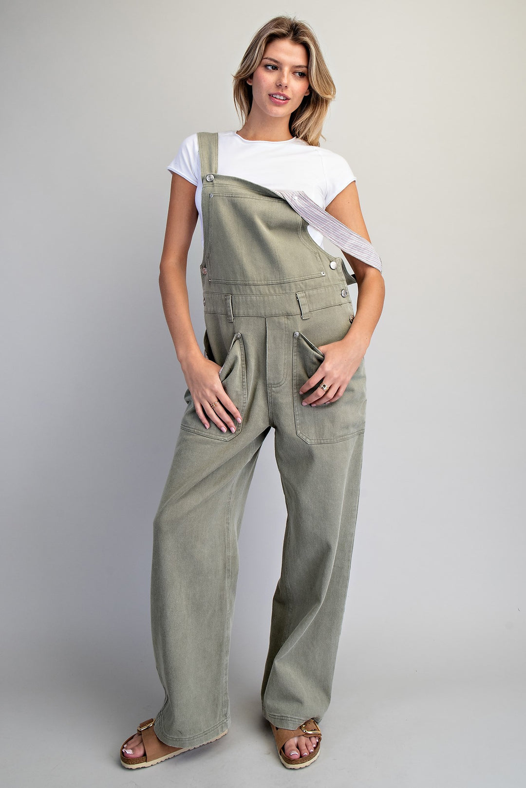 Woman wearing green overalls and white tee on plain background