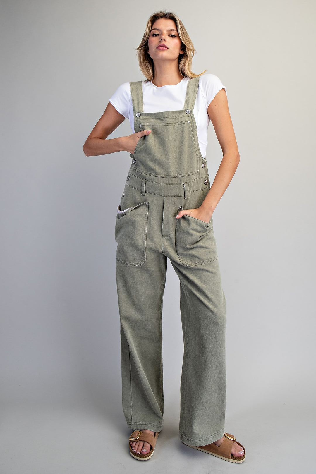 Woman wearing green overalls and a white shirt on a plain background