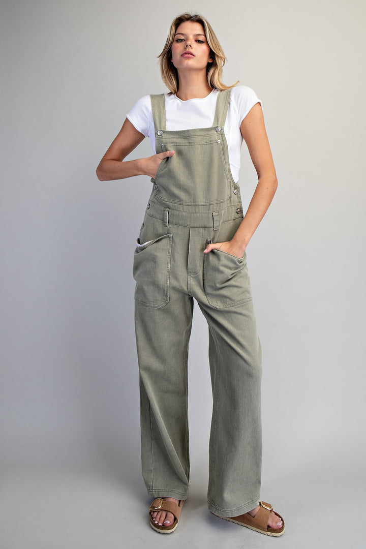 Woman wearing green overalls and a white shirt on a plain background