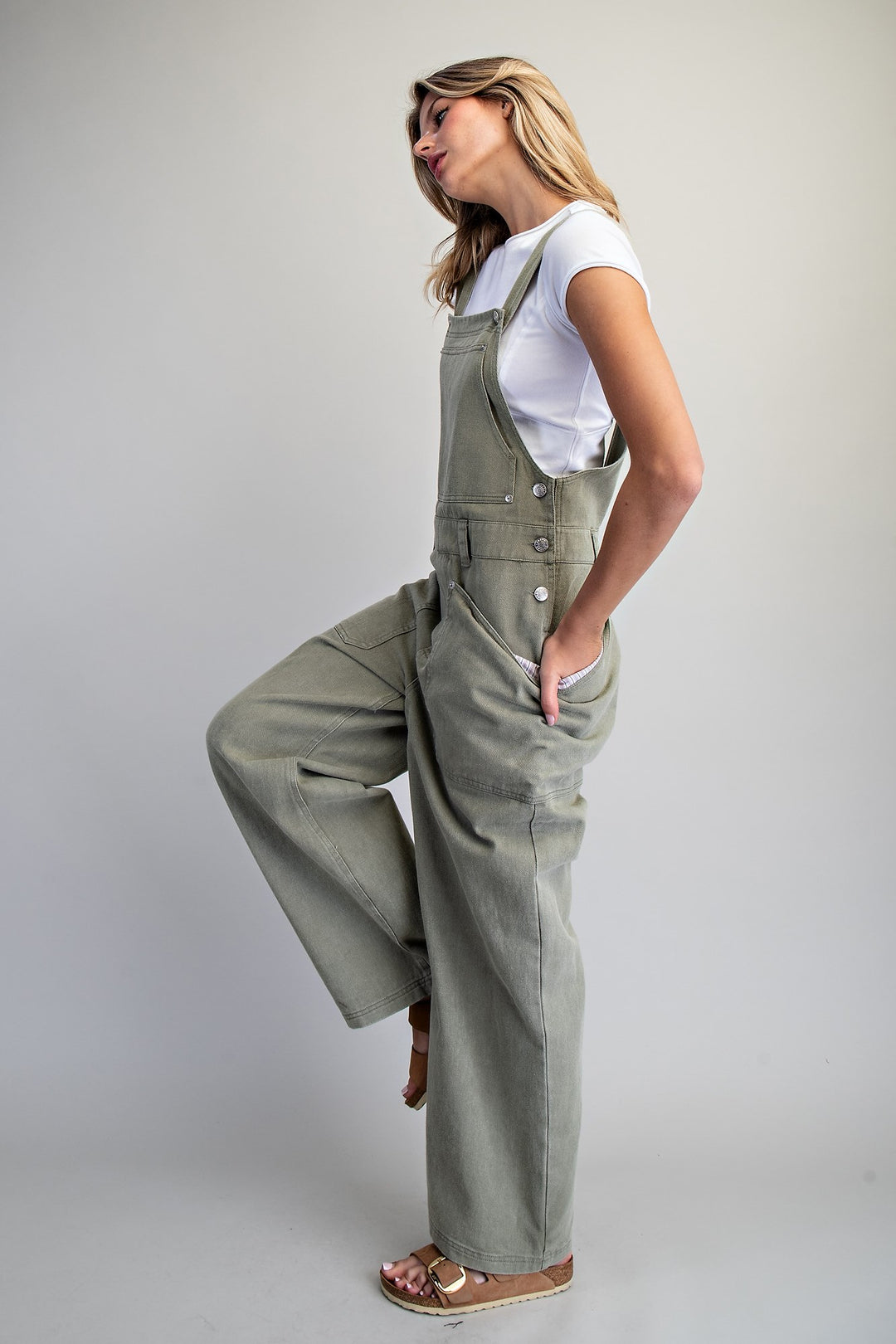 Woman wearing green overalls and a white shirt on a plain background