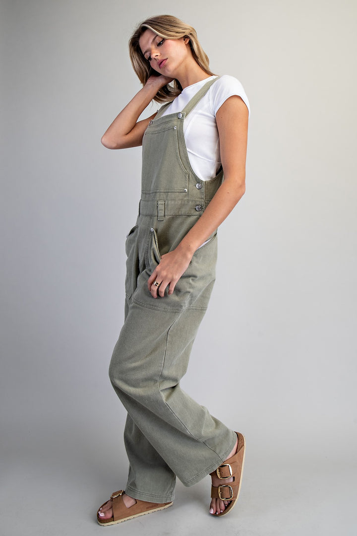 Woman wearing green overalls and a white shirt on a plain background