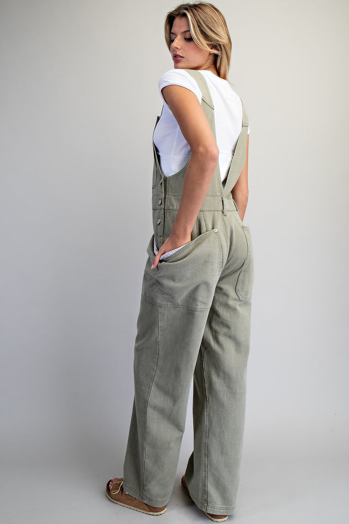 Woman wearing green overalls and white tee on plain background
