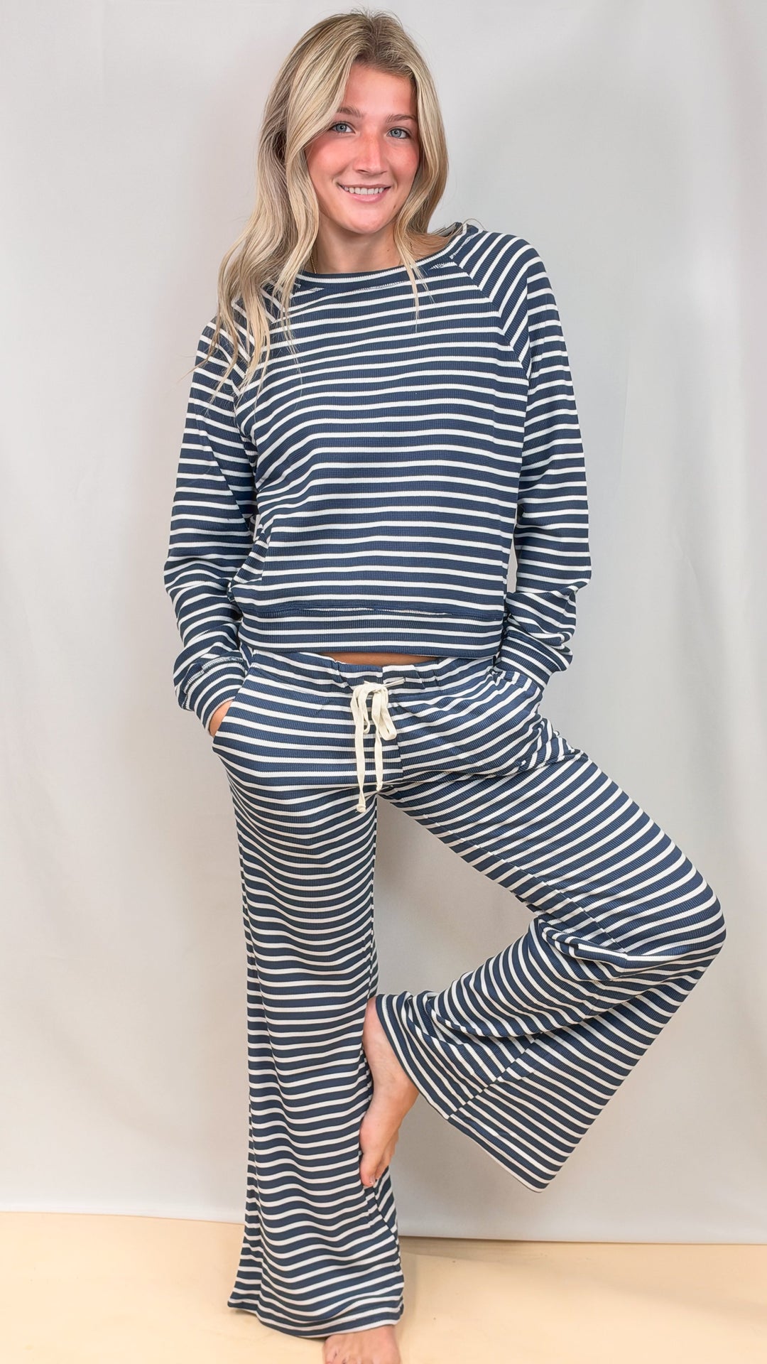 Woman wearing matching blue and white stripe long sleeve top and pant set on plain background