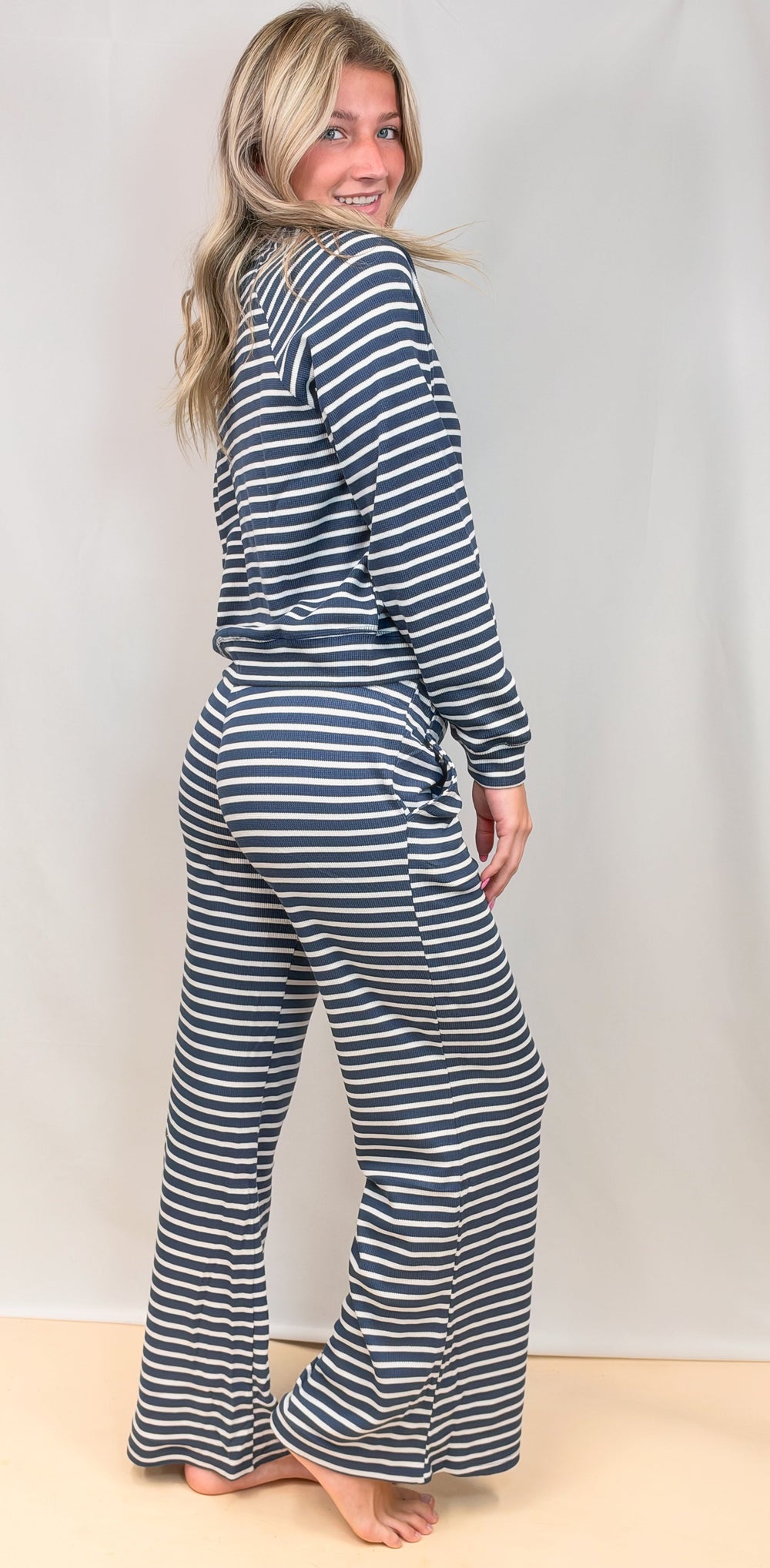 Woman shown from side view wearing navy and white stripe long sleeve and pant set on plain background