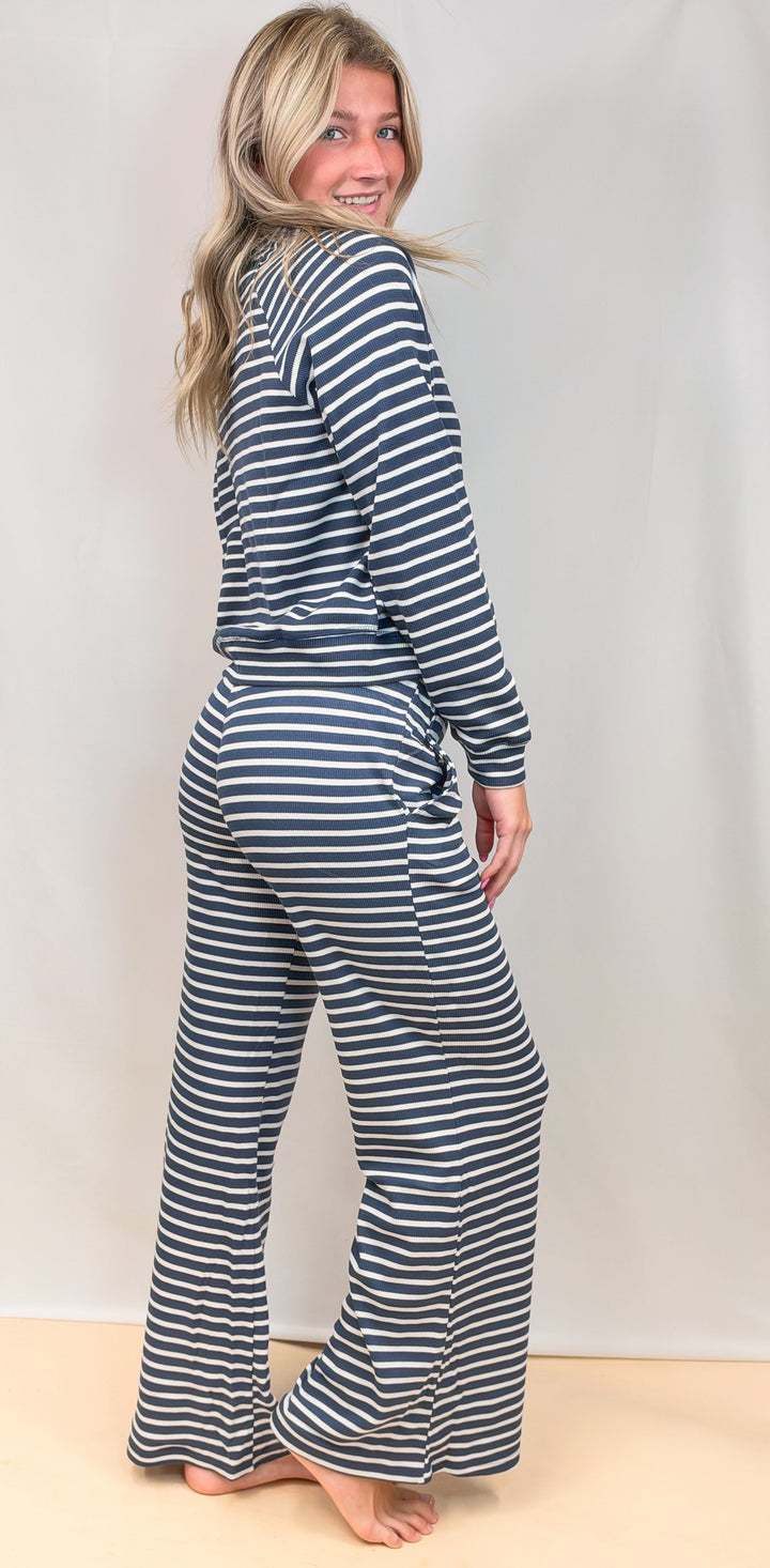 Woman shown from side view wearing navy and white stripe long sleeve and pant set on plain background