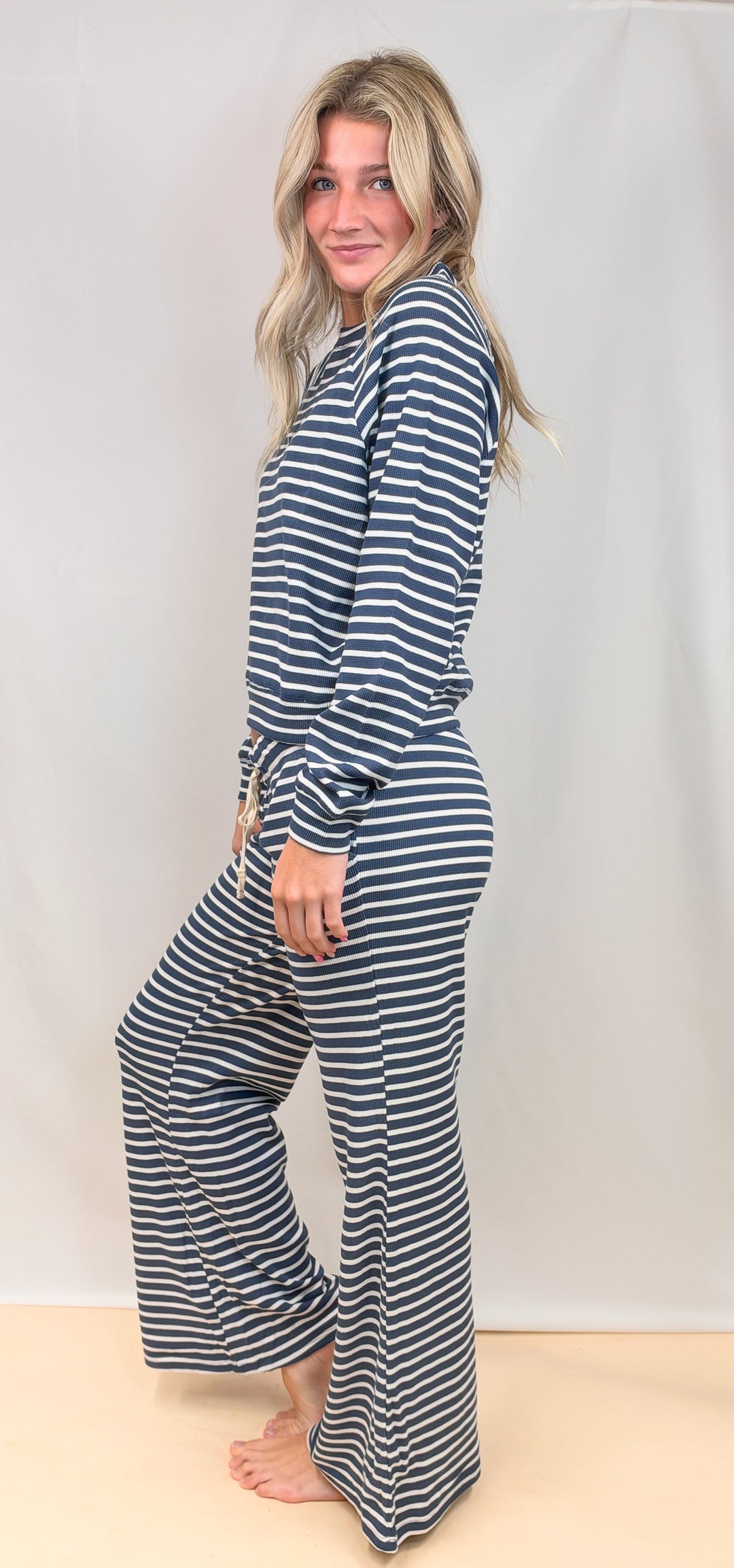 Woman shown from side view wearing matching long sleeve top and pant navy and white stripe set on plain background