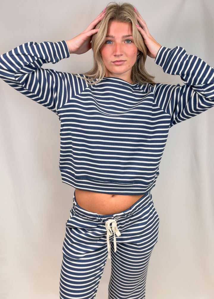 Woman wearing matching navy and white stripe long sleeve top and pant set on plain background
