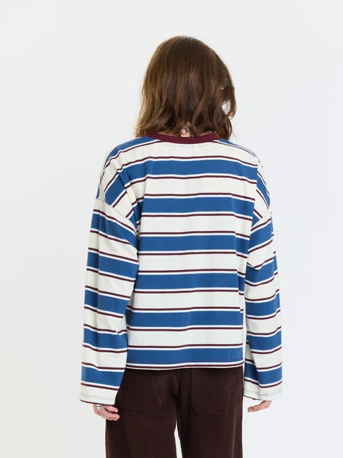 A person shown from the back wearing a long-sleeve striped shirt with blue, white, and thin red stripes, paired with dark brown pants, against a plain white background.