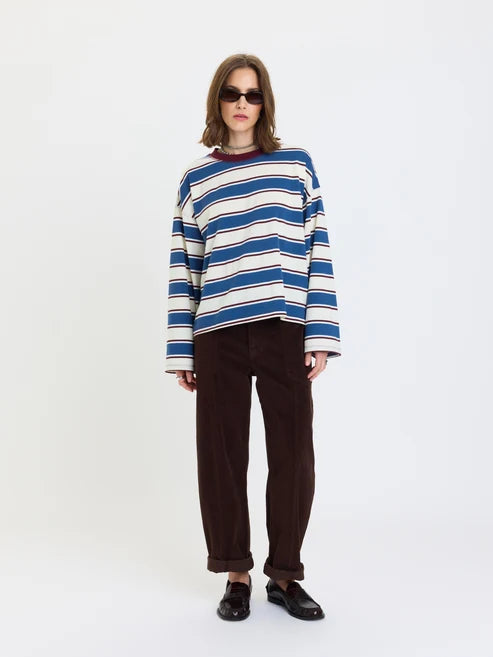 A model wearing a blue, white, and navy striped long-sleeve knit sweater, dark brown corduroy pants, and black loafers, standing against a plain white studio background.