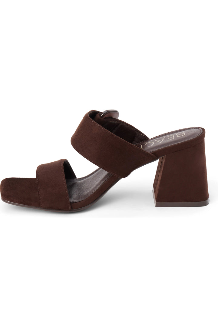 A dark brown suede mule sandal with a chunky block heel and double straps, shown from a side profile on a white background.