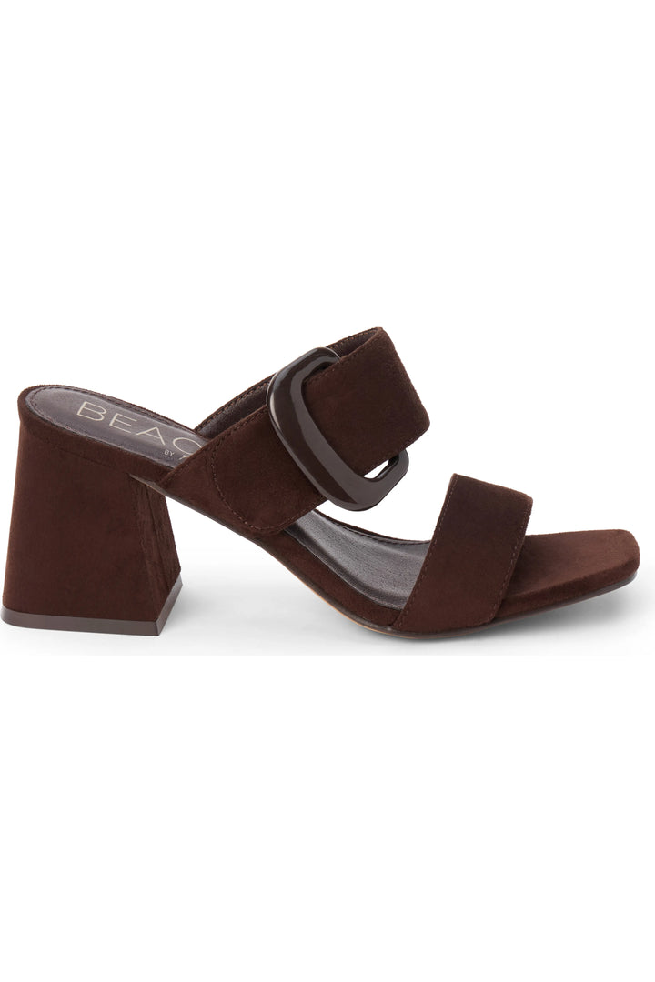 A dark brown suede block-heel slide sandal with a wide strap and a large square buckle, shown from a side profile on a white background.