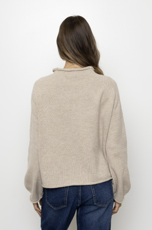 Woman shown from behind wearing oatmeal colored sweater and jeans on plain background