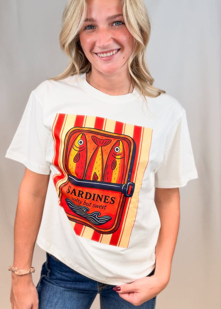 Woman wearing white graphic tee with sardines on front with jeans on plain background