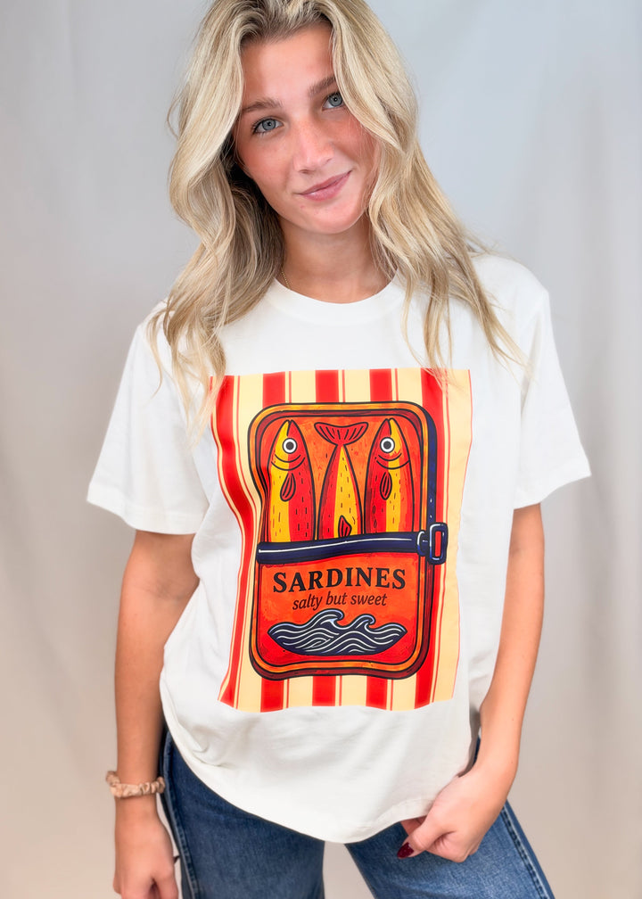 Woman wearing white graphic tee with sardines on front with jeans on plain background