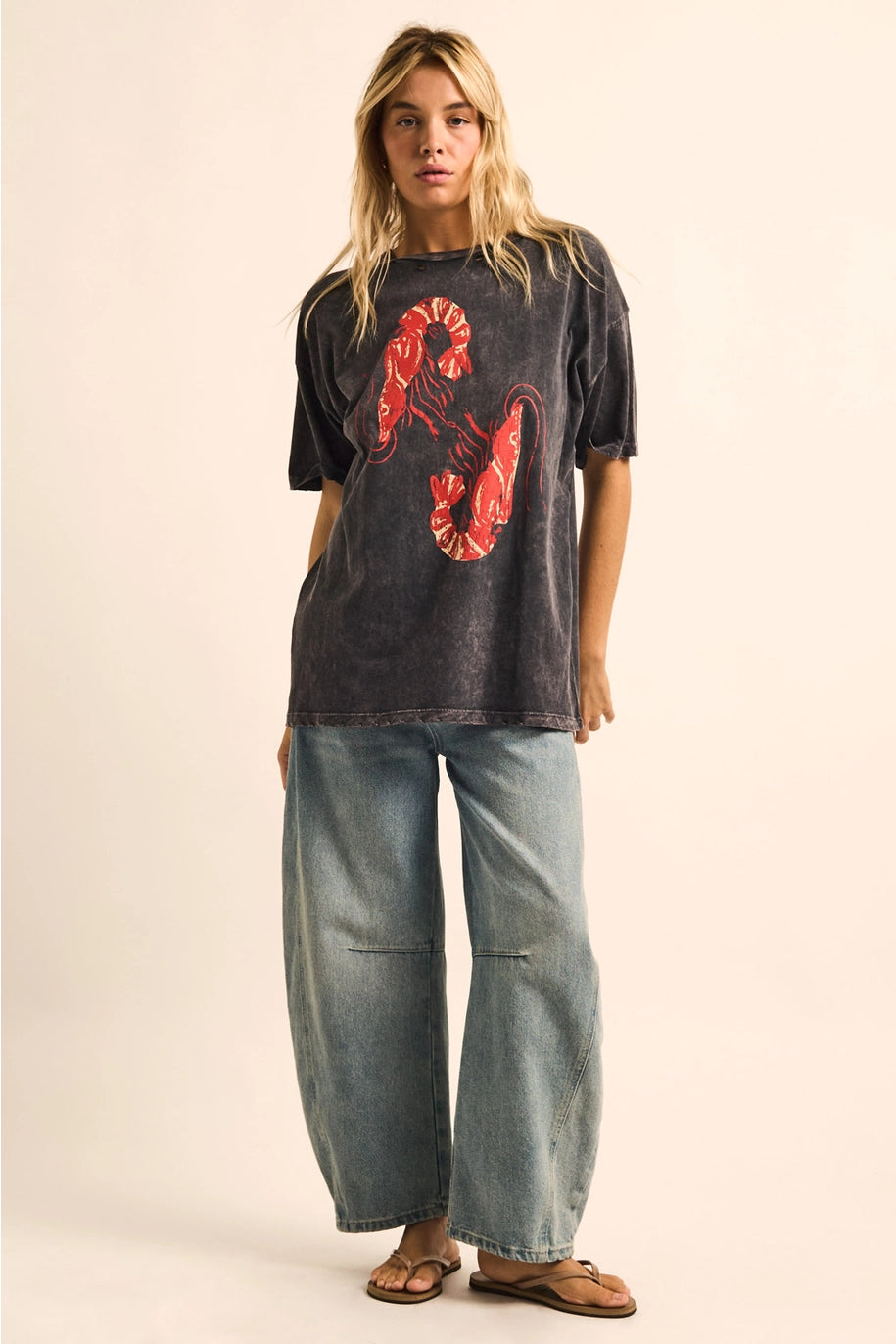 Person wearing a dark t-shirt with red graphics and light blue jeans on a beige background