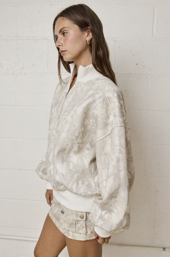 Woman wearing a white tie-dye jacket against a white brick wall.