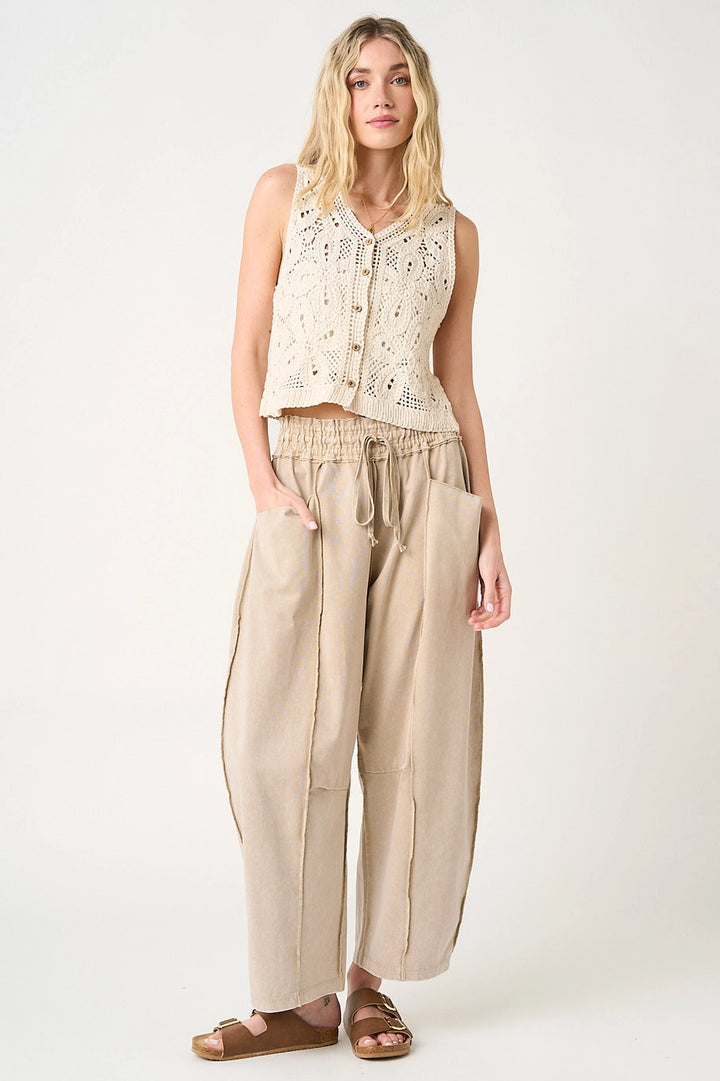 Woman wearing a sleeveless beige top and wide-leg pants on a white background
