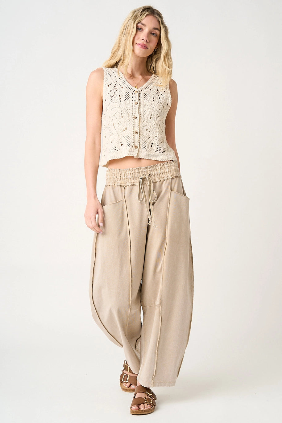 Woman wearing a sleeveless lace top and beige wide-leg pants on a white background