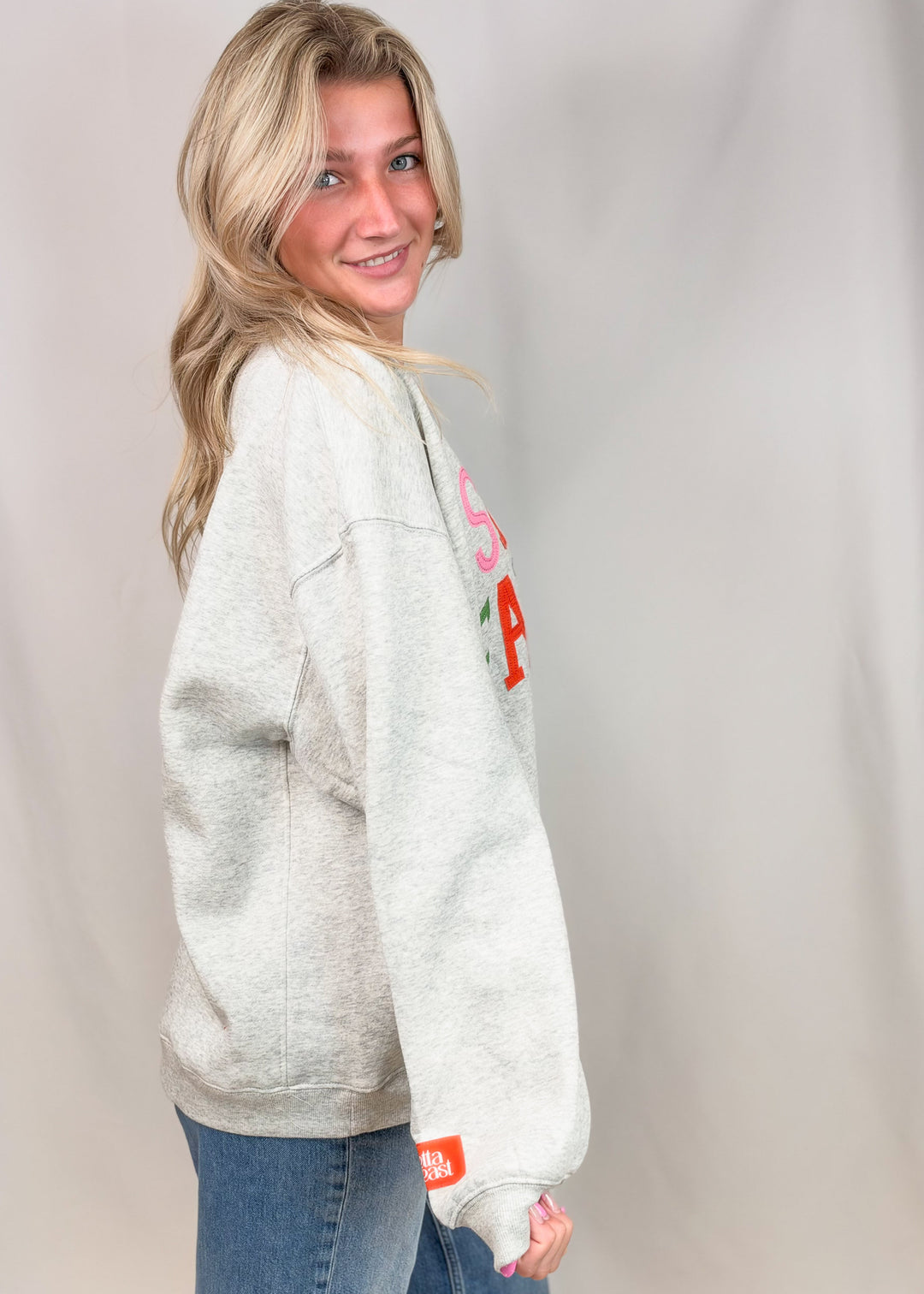 Woman shown from side view wearing grey sweatshirt and jeans on plain background