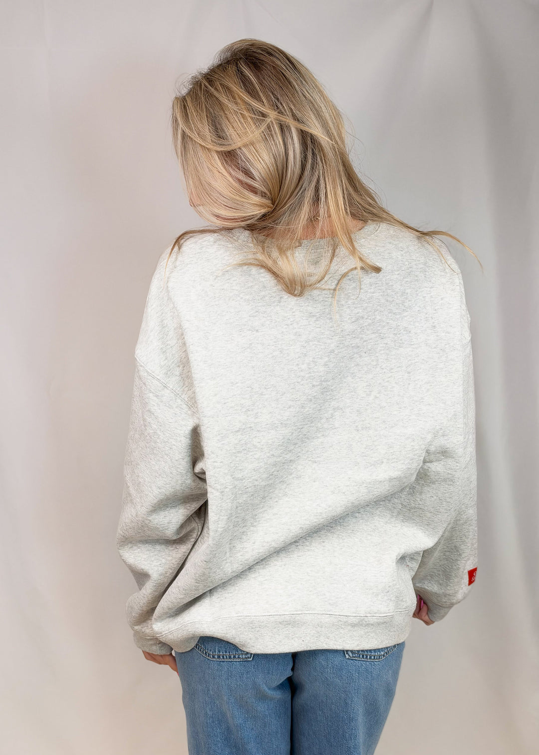 Woman shown from back wearing grey sweatshirt and jeans on plain background