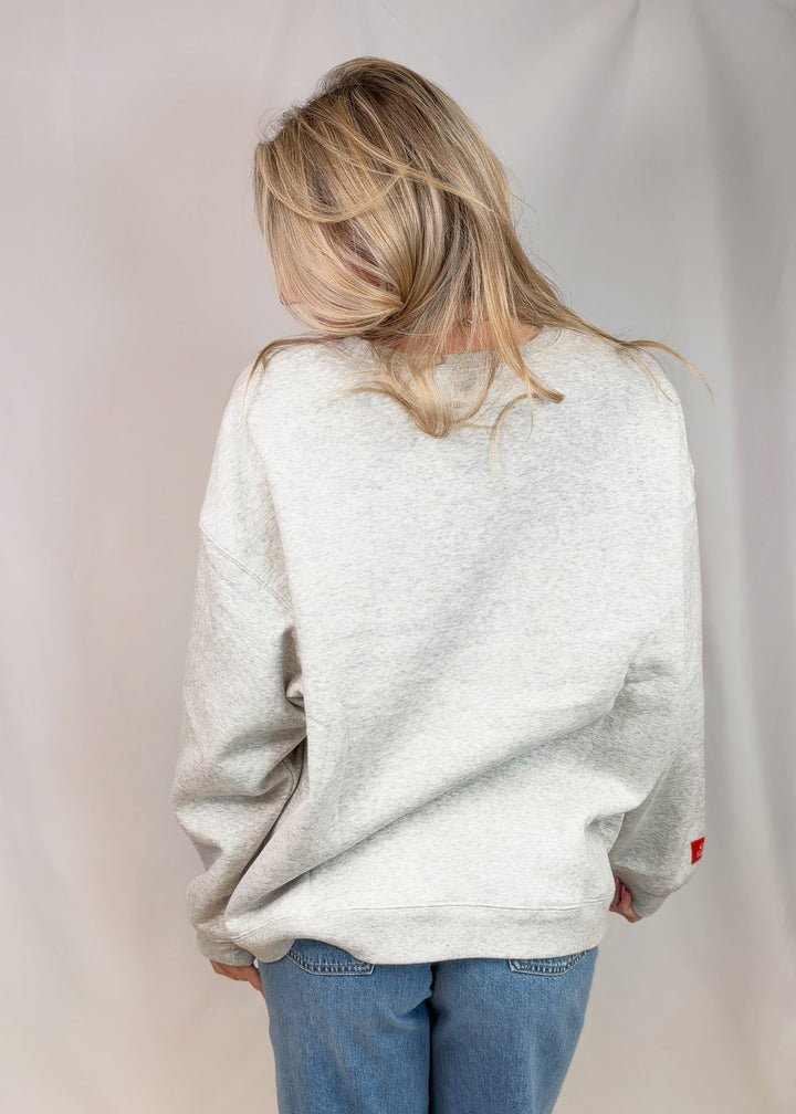 Woman shown from back wearing grey sweatshirt and jeans on plain background