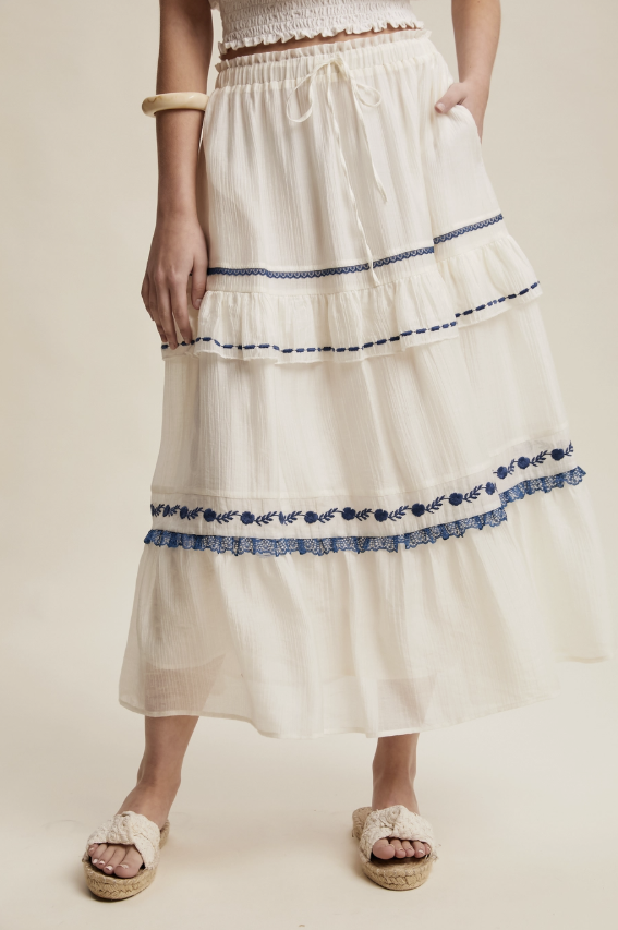 Woman wearing a white skirt with blue embroidery on a beige background