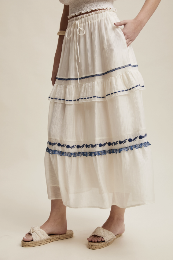White tiered skirt with blue embroidery on a plain background