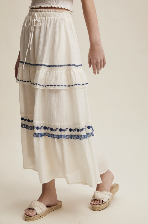 White skirt with blue embroidery worn by a person on a plain background