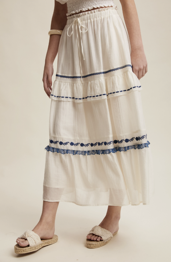 White tiered skirt with blue embroidery on a neutral background